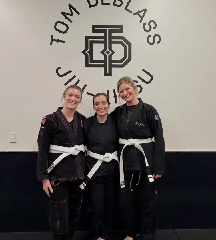 Three women in their gis with white belts smiling after class at Flow BJJ in Rockland, Maine