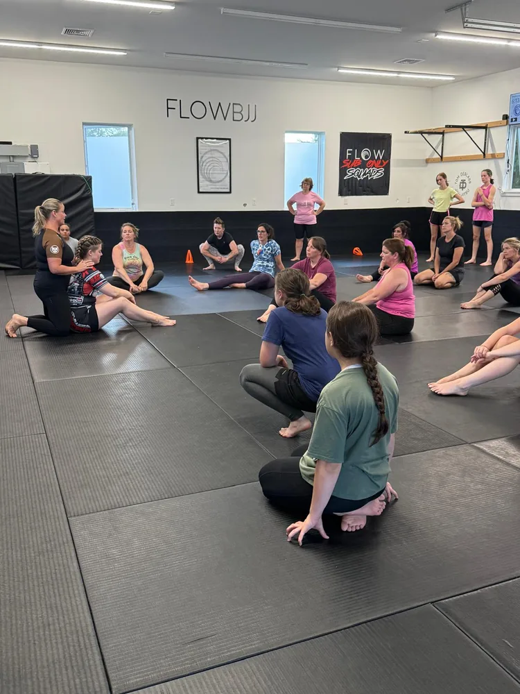 Coach Sandy teaching technique to women seated in a circle at Flow BJJ